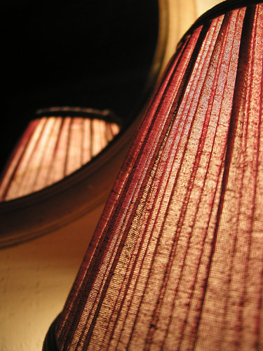 Close-up picture of red and black pleated mini lampshade illuminated and reflected in a hotel mirror.